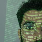 Rosto de um homem sobreposto por códigos binários, em referência à tecnologia digital e à cibersegurança