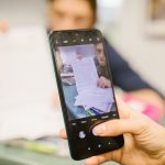 Estudante usa um celular para fotografar folhas de uma prova em uma sala de aula.