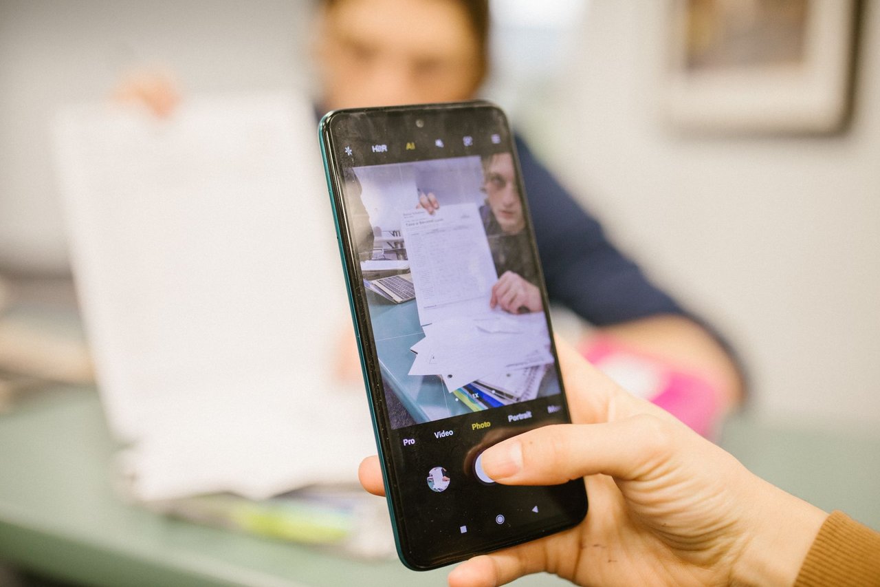 Estudante usa um celular para fotografar folhas de uma prova em uma sala de aula.