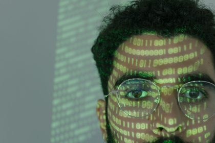 Rosto de um homem sobreposto por códigos binários, em referência à tecnologia digital e à cibersegurança
